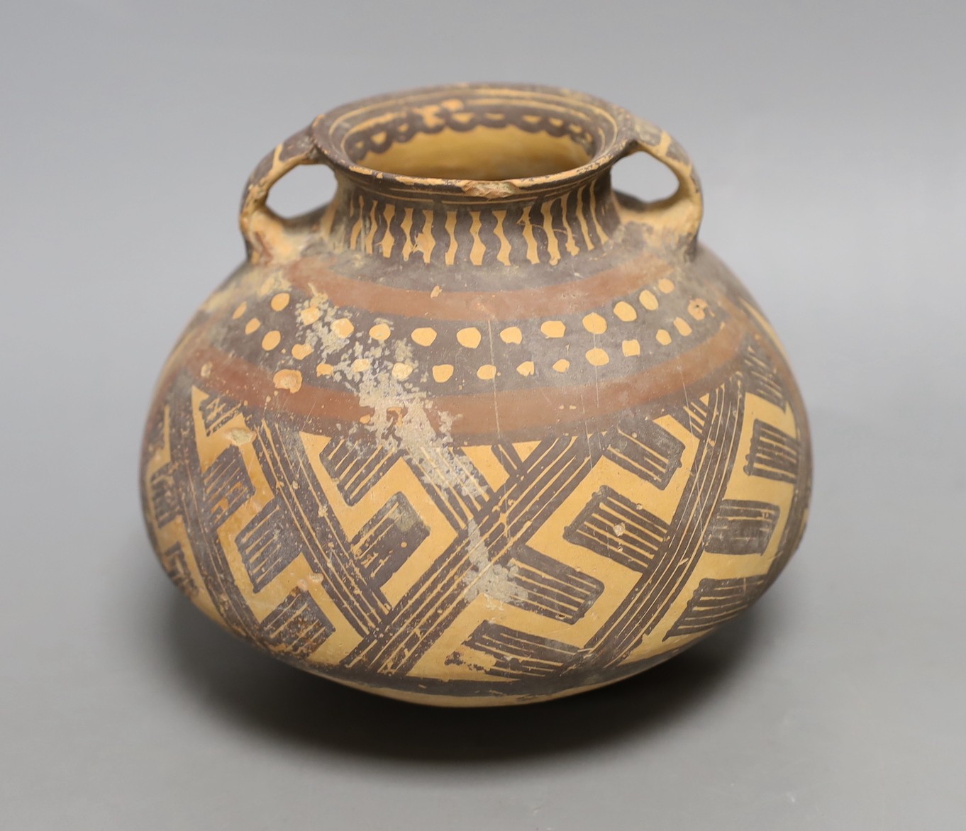 A Chinese pigment painted pottery two handled jar, possibly Neolithic, 14cm high